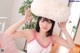 A woman in a white tank top holding a fluffy white hat.